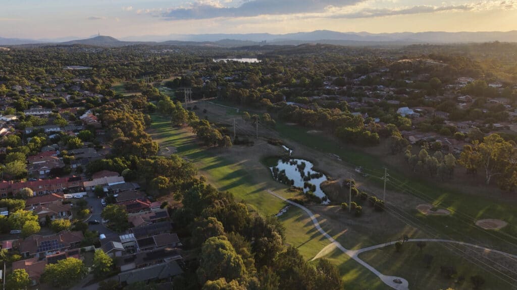 Aerial view of a golf course at sunset with houses and trees in the background.
